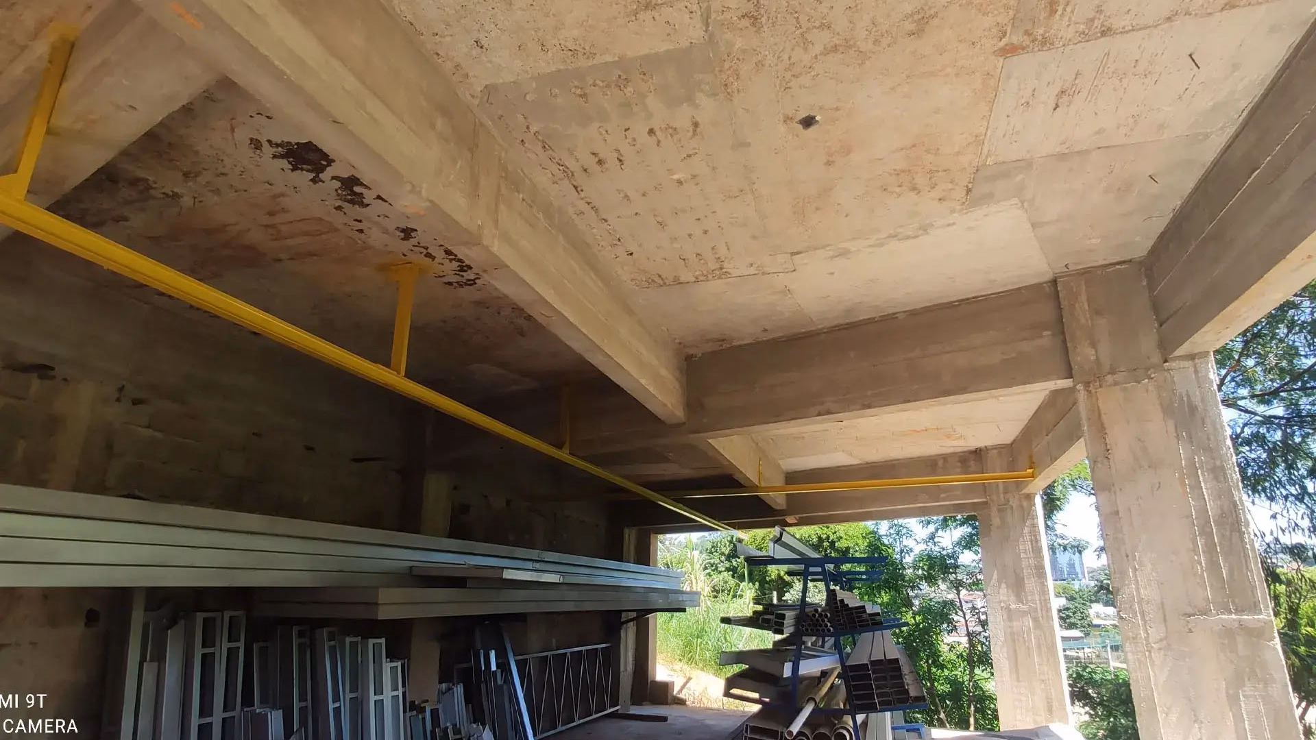 Interior industrial mostrando teto de concreto robusto e tubulações aparentes pintadas, foco em infraestrutura